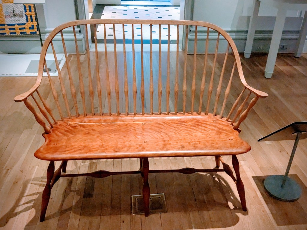 A bench-sized seat of wood placed on display in a museum.